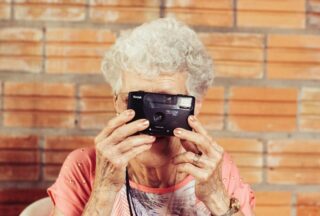 Une grand-mère prend une photo avec un appareil photo avec un mur en brique en fond